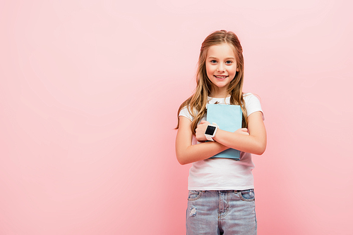 child in white t-shirt and smartwatch  while holding book isolated on pink