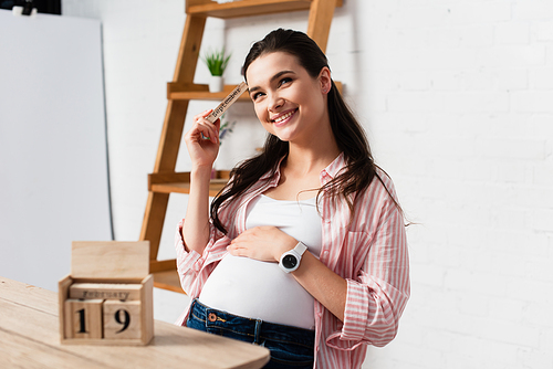 selective focus of pregnant woman touching belly near wooden cubes with date