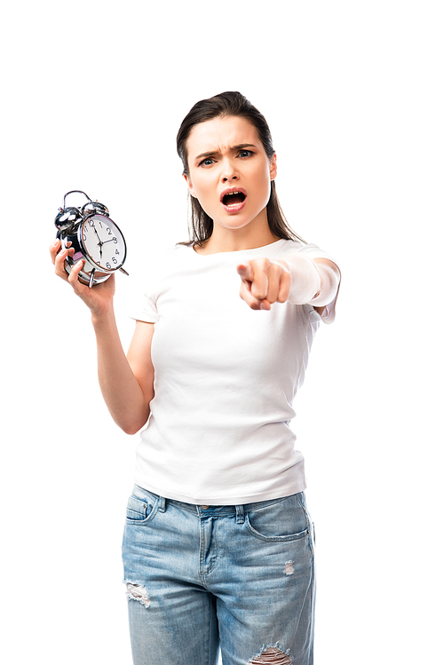 selective focus of woman in white t-shirt and jeans holding retro alarm clock while pointing with finger isolated on white