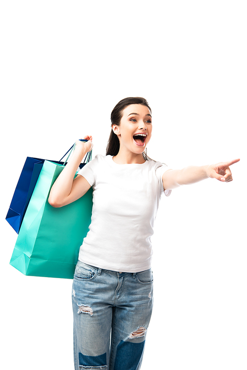 young brunette woman holding shopping bags and pointing with finger isolated on white