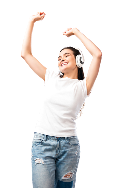 young woman in white t-shirt and wireless headphones dancing with hands above head isolated on white