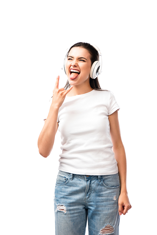 woman in wireless headphones sticking out tongue while showing rock sign isolated on white