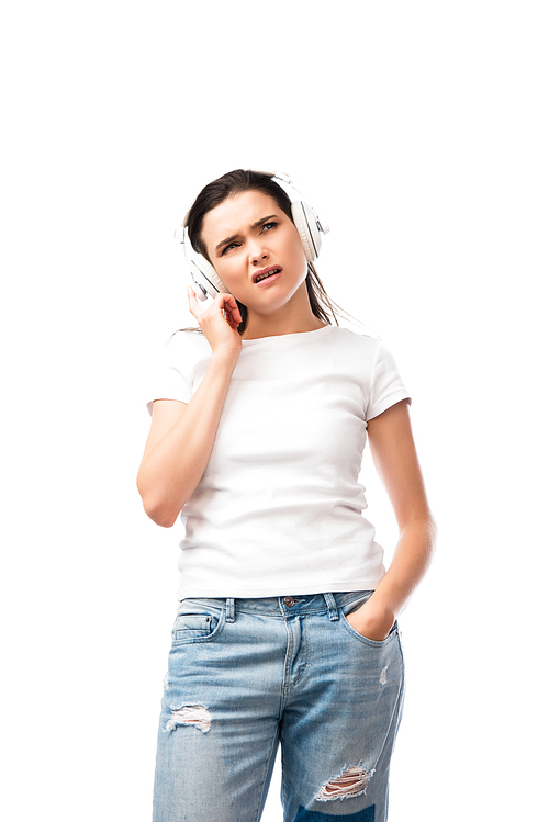 pensive woman in white t-shirt and wireless headphones standing with hand in pocket isolated on white