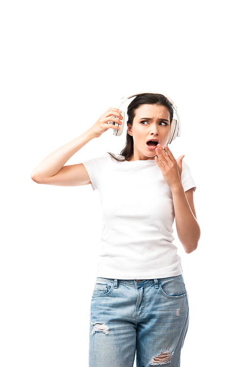 shocked young woman in white t-shirt touching wireless headphones isolated on white