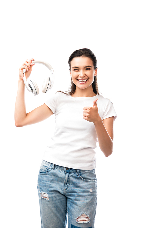 young woman in white t-shirt holding wireless headphones and showing thumb up isolated on white