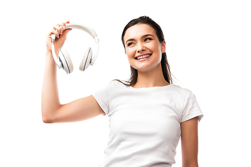 young woman in white t-shirt looking at wireless headphones isolated on white