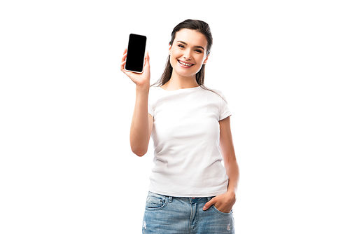 young woman in white t-shirt standing with hand in pocket and holding smartphone with blank screen isolated on white