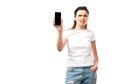 displeased woman standing with hand in pocket and looking at smartphone with blank screen isolated on white