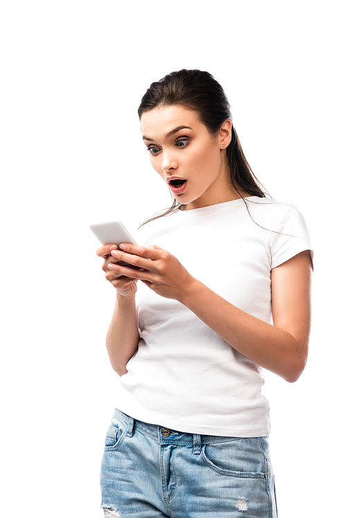 shocked brunette woman in white t-shirt using smartphone isolated on white