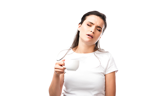 sleepy brunette woman in white t-shirt holding cup with coffee isolated on white