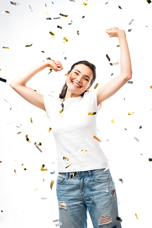 excited woman in white t-shirt with hands above head near confetti on white