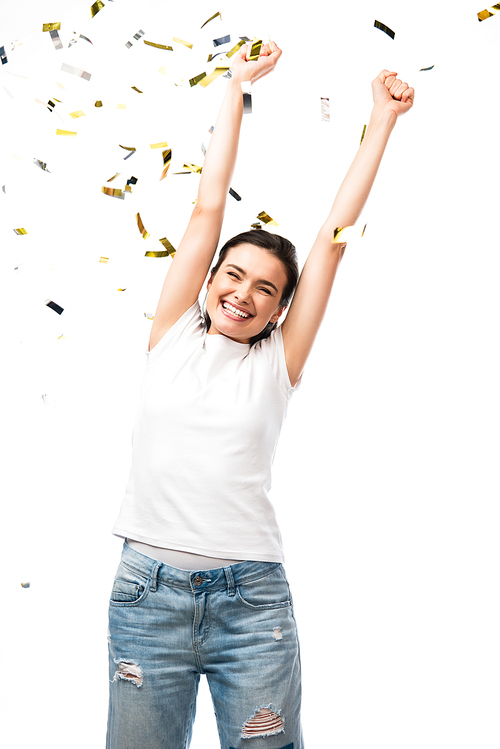 excited young woman in white t-shirt with hands above head near confetti on white