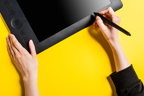 cropped view of designer holding black stylus near drawing tablet with blank screen on yellow