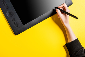 cropped view of designer holding modern stylus near drawing tablet with blank screen on yellow