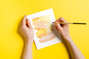 cropped view of woman holding paintbrush near painting on yellow