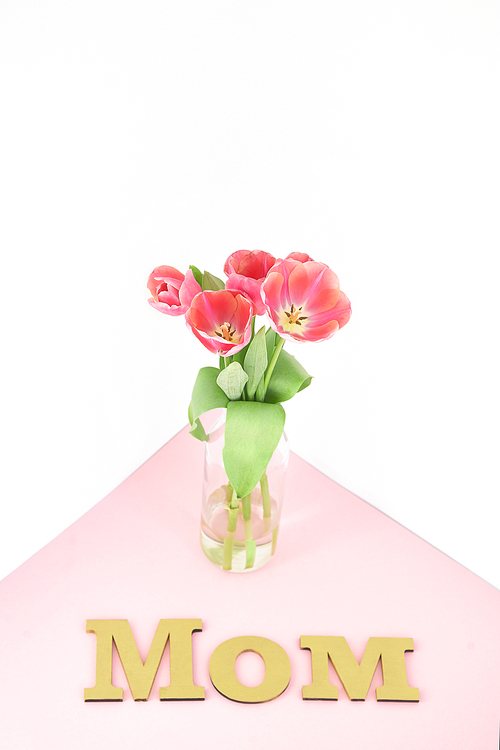 spring tulips in vase near mom lettering on pink and white background