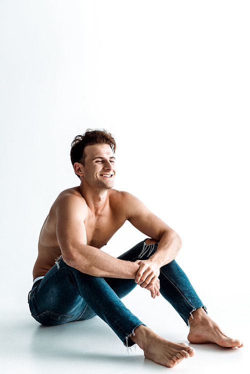 cheerful shirtless man with barefoot sitting on white