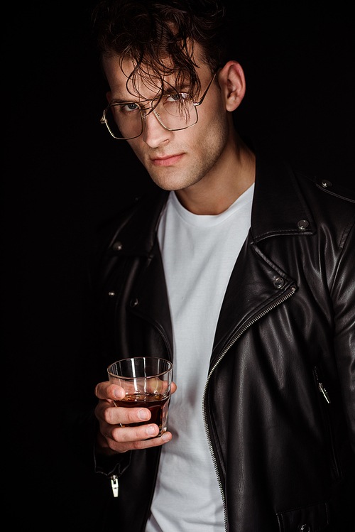 trendy man in eye glasses holding glass with whiskey isolated on black