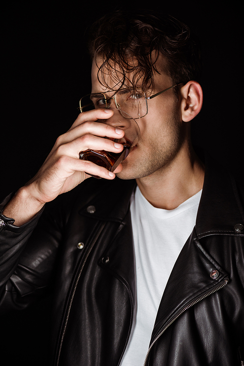 trendy man holding glass and drinking whiskey isolated on black