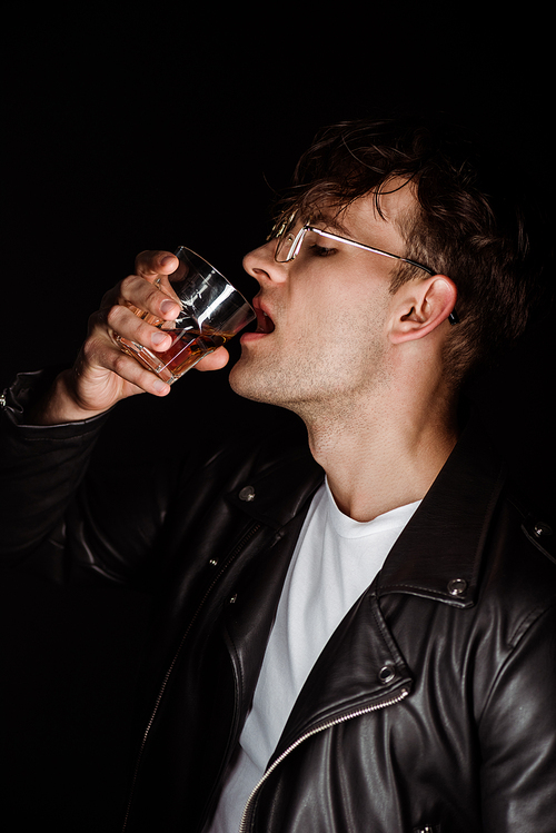 brutal man holding glass and drinking whiskey isolated on black