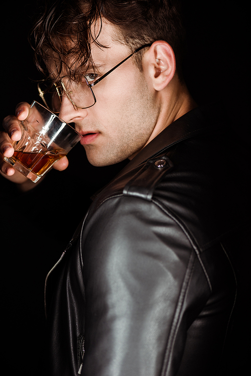 brutal man in eye glasses holding glass with whiskey isolated on black