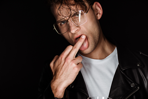 brutal man in glasses showing middle finger while sticking out tongue isolated on black