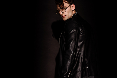 trendy man in glasses and leather jacket standing on black