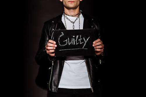 cropped view of man holding chalk board with guilty lettering on black