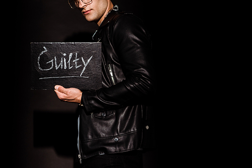 cropped view of young man holding chalk board with guilty lettering on black