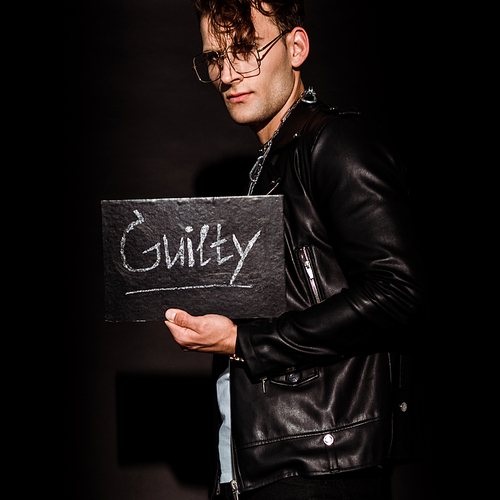 handsome man holding chalk board with guilty lettering on black