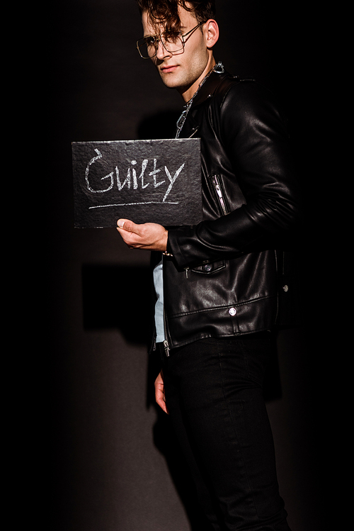 stylish man holding chalk board with guilty lettering on black