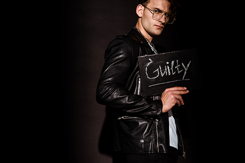 stylish man in glasses holding chalk board with guilty lettering on black