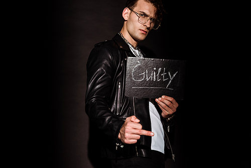 handsome man in glasses holding chalk board with guilty lettering on black