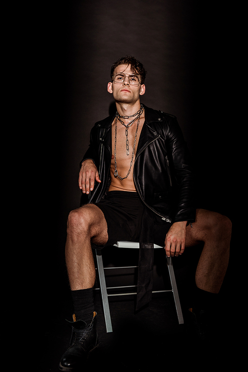 brutal young man in leather jacket sitting on black