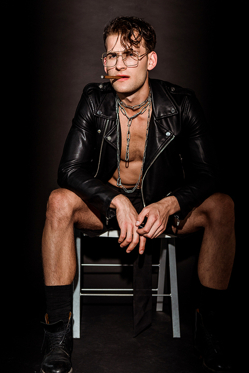 brutal man in leather jacket sitting on chair with cigar on black