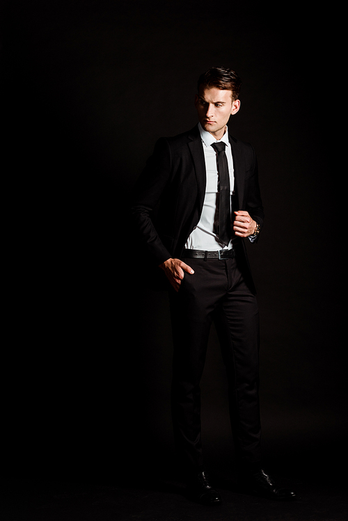 handsome businessman in suit standing with hand in pocket on black