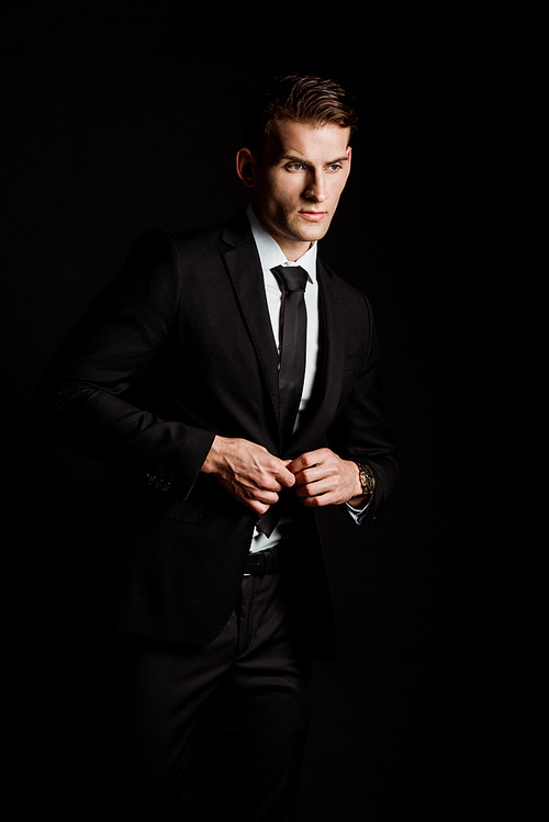 confident businessman touching formal wear isolated on black