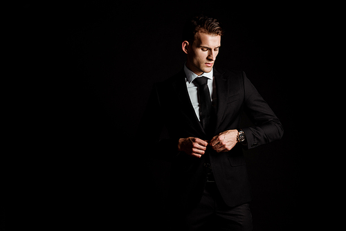 confident man touching formal wear isolated on black