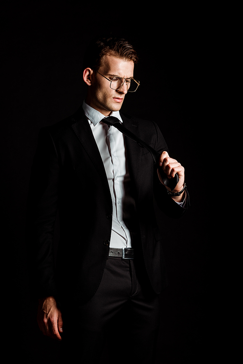 businessman in glasses looking at tie isolated on black