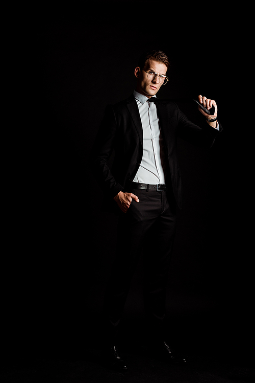 businessman in glasses holding tie isolated on black