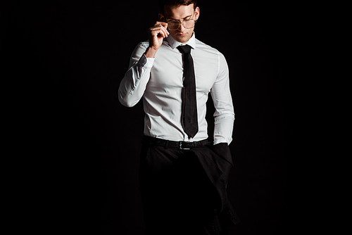 handsome businessman touching glasses isolated on black