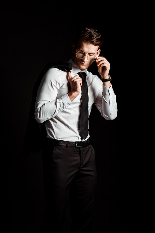 handsome man touching glasses isolated on black