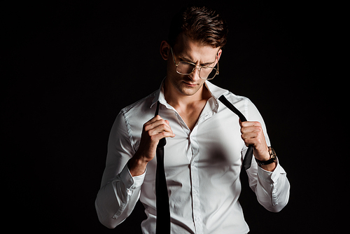 handsome businessman in glasses taking off tie isolated on black