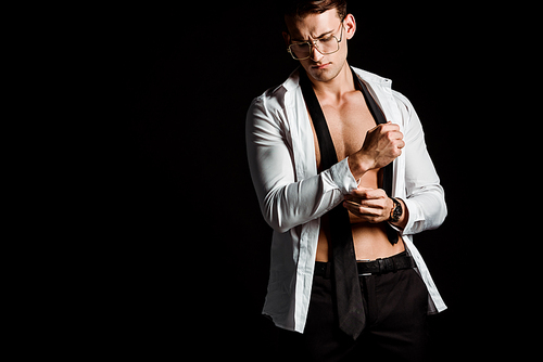 undressed man in glasses standing and touching suit isolated on black