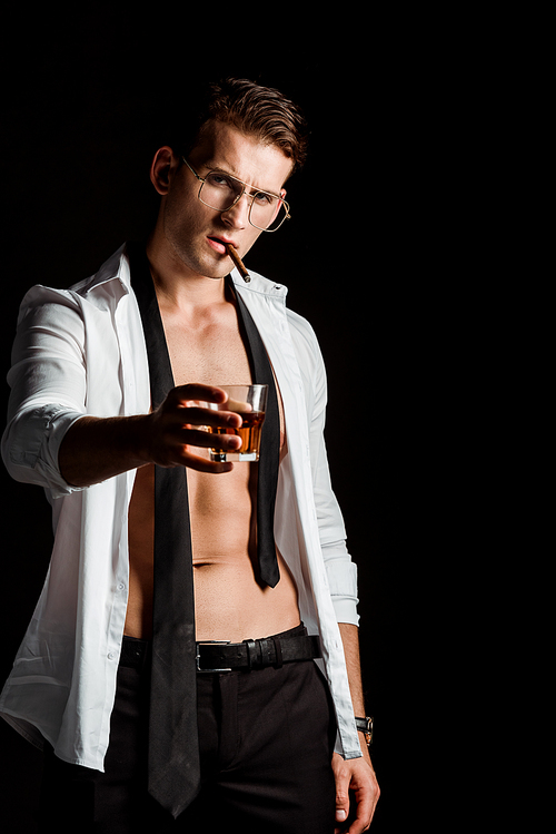 man in suit holding glass with whiskey while smoking isolated on black