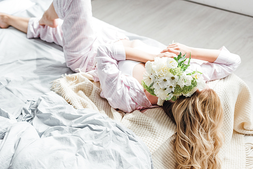 young woman covering face with flowers while lying on bed