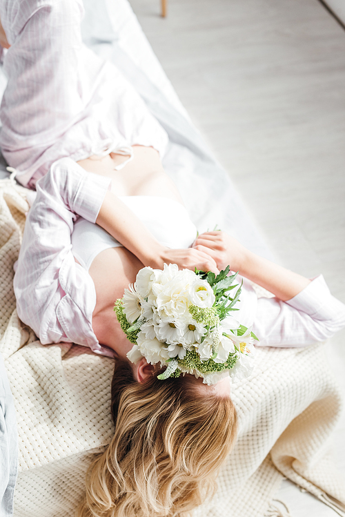 girl covering face with flowers while lying on bed