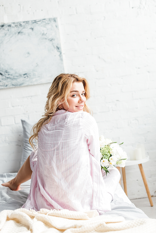 selective focus of pretty girl sitting on bed with flowers