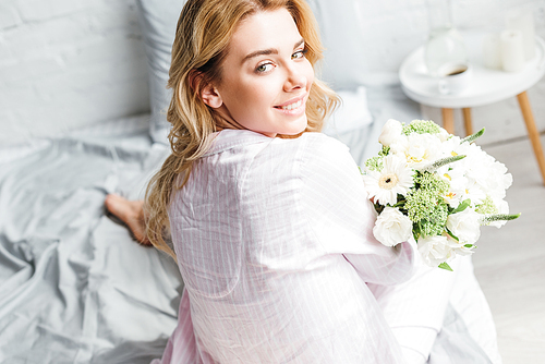 selective focus of pretty woman sitting on bed with flowers