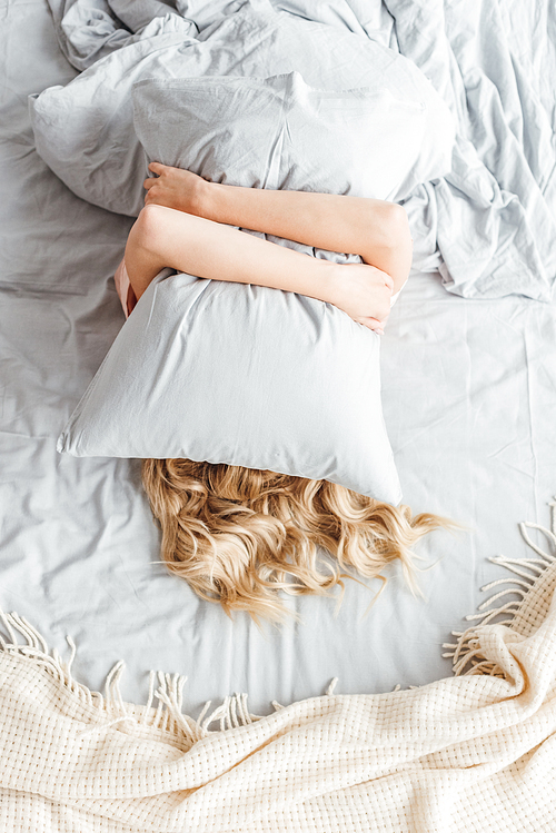 top view of woman covering face with pillow in bedroom